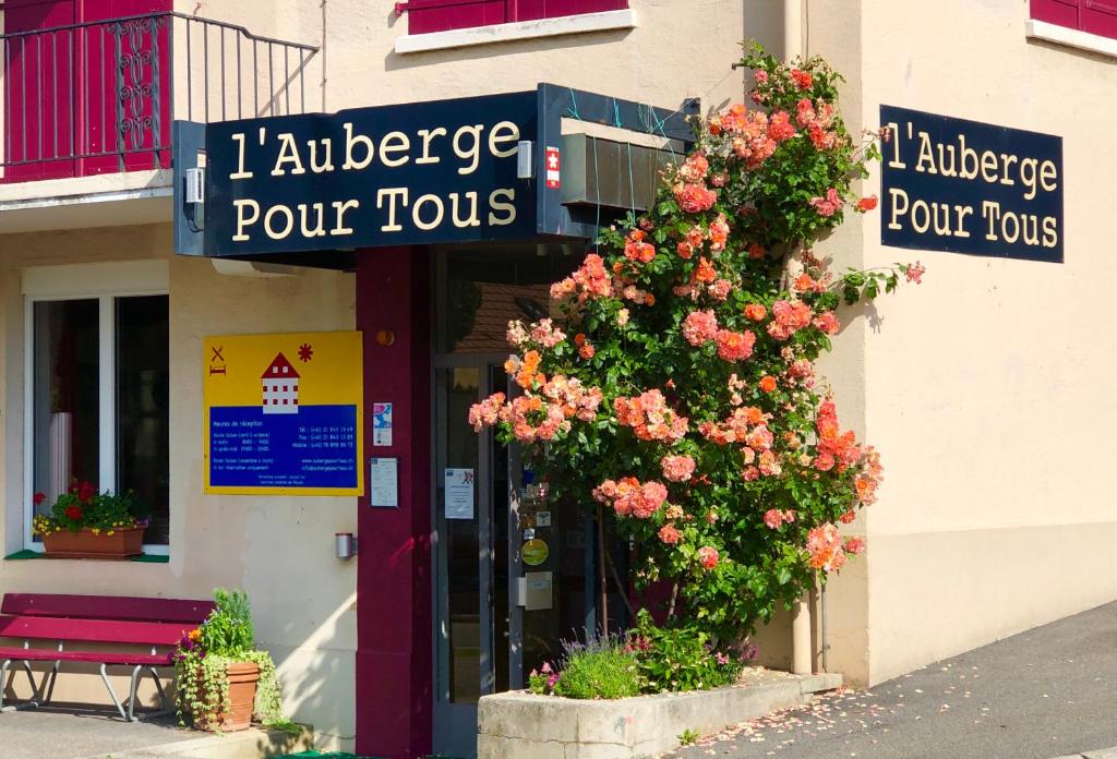 un bâtiment avec une brousse fleurie devant un magasin dans l'établissement Auberge Pour Tous, à Vallorbe