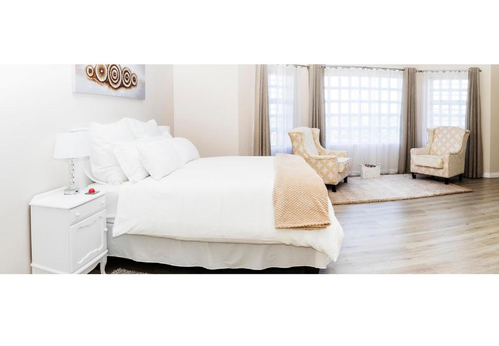 a white bedroom with a large bed and two chairs at Settle Inn Self Catering Accommodation in Colchester