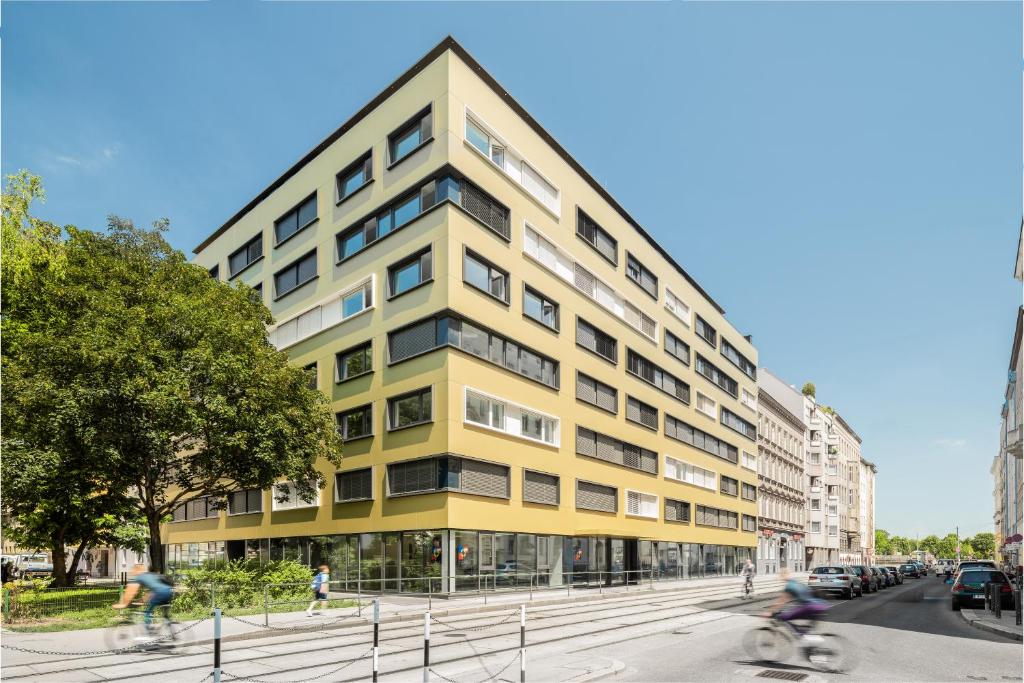 ein gelbes Gebäude auf einer Stadtstraße mit Menschen, die Fahrrad fahren in der Unterkunft myNext - Hotel Leo in Wien