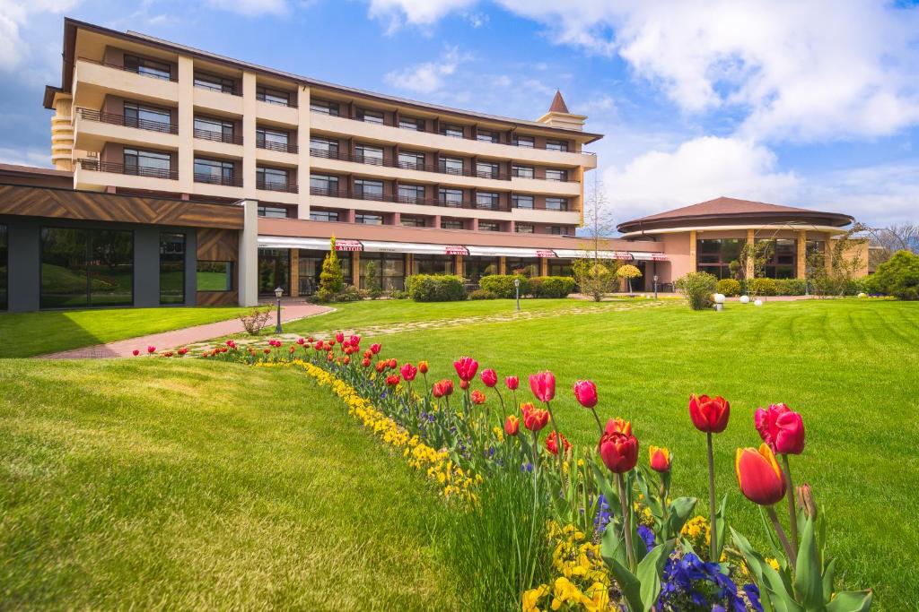 a building with a field of flowers in front of it at Hotel Sevtopolis Medical & SPA in Pavel Banya