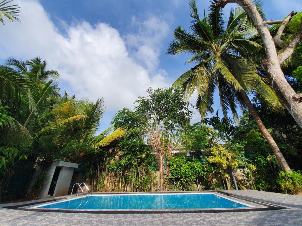 a swimming pool with palm trees in the background at Mihin Villa in Bentota