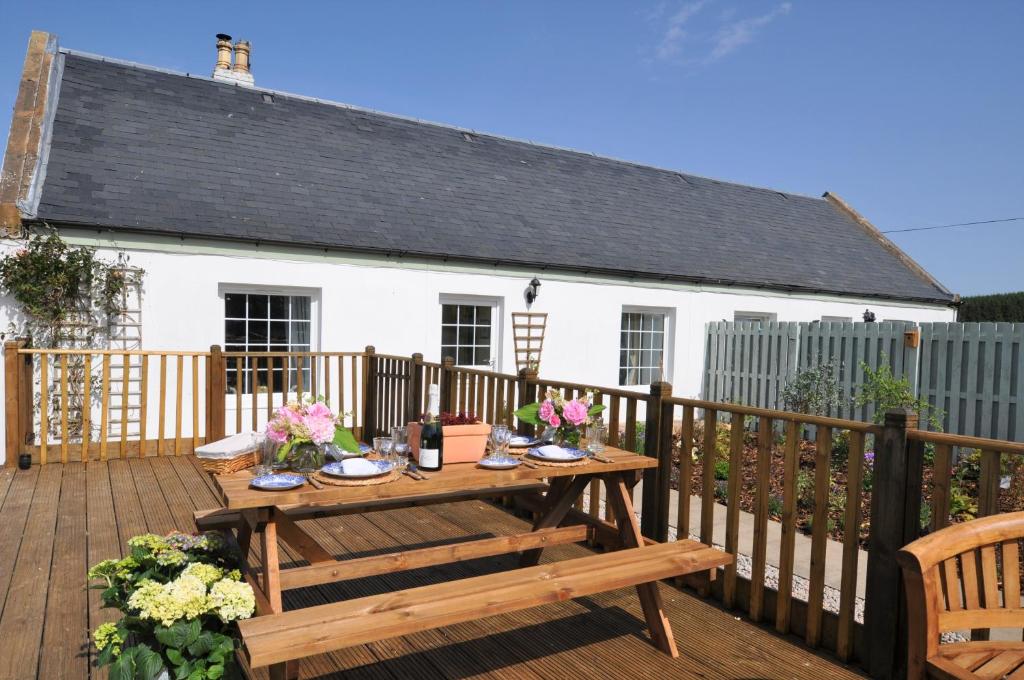 a wooden deck with a table and a white house at No 1 Ramageton in Hurlford