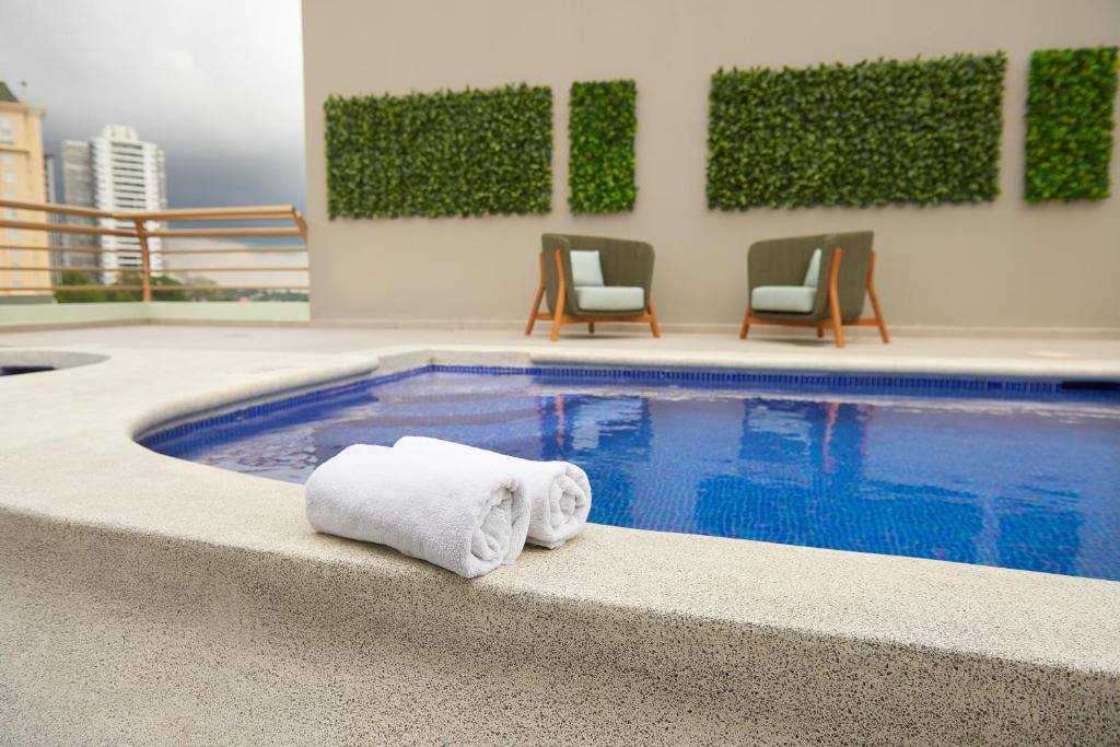 uma piscina com duas toalhas e cadeiras num edifício em Suites las Palmas, Hotel & Apartments. em San Salvador