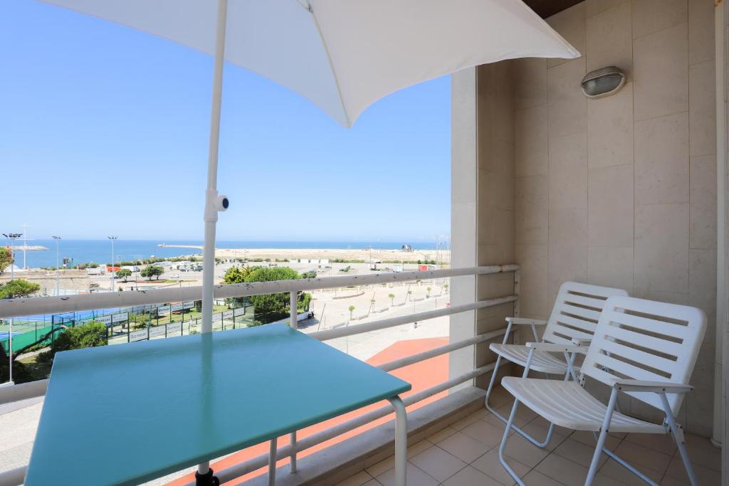 uma varanda com uma mesa e cadeiras azuis e um guarda-sol em Sea View Apartment na Figueira da Foz