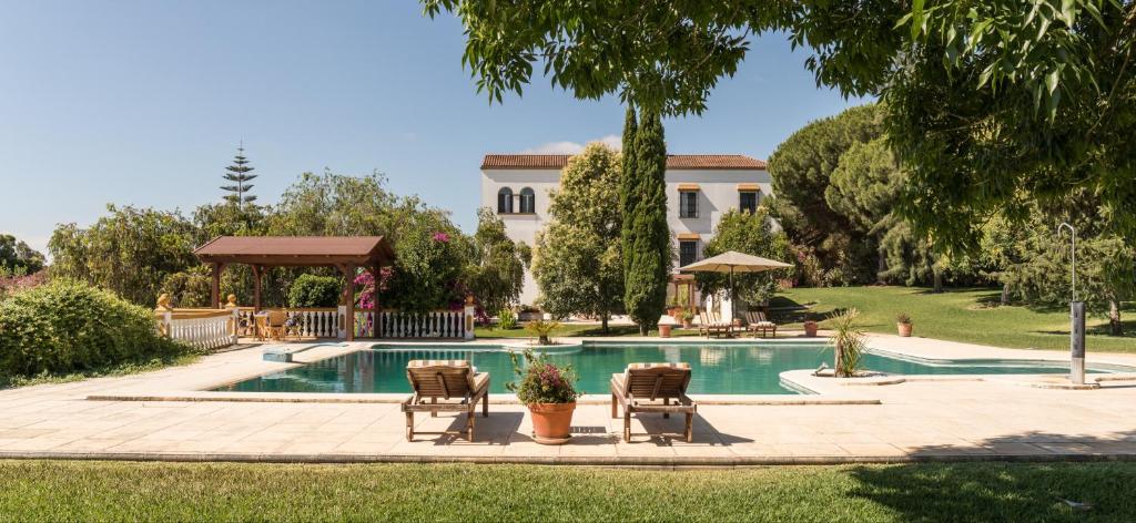 una piscina con sillas y una casa en el fondo en Hacienda las tres niñas, en La Puebla del Río