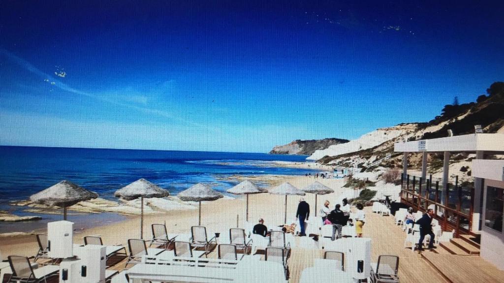 una playa con sillas y sombrillas blancas y el océano en oasi scala dei turchi, en Realmonte