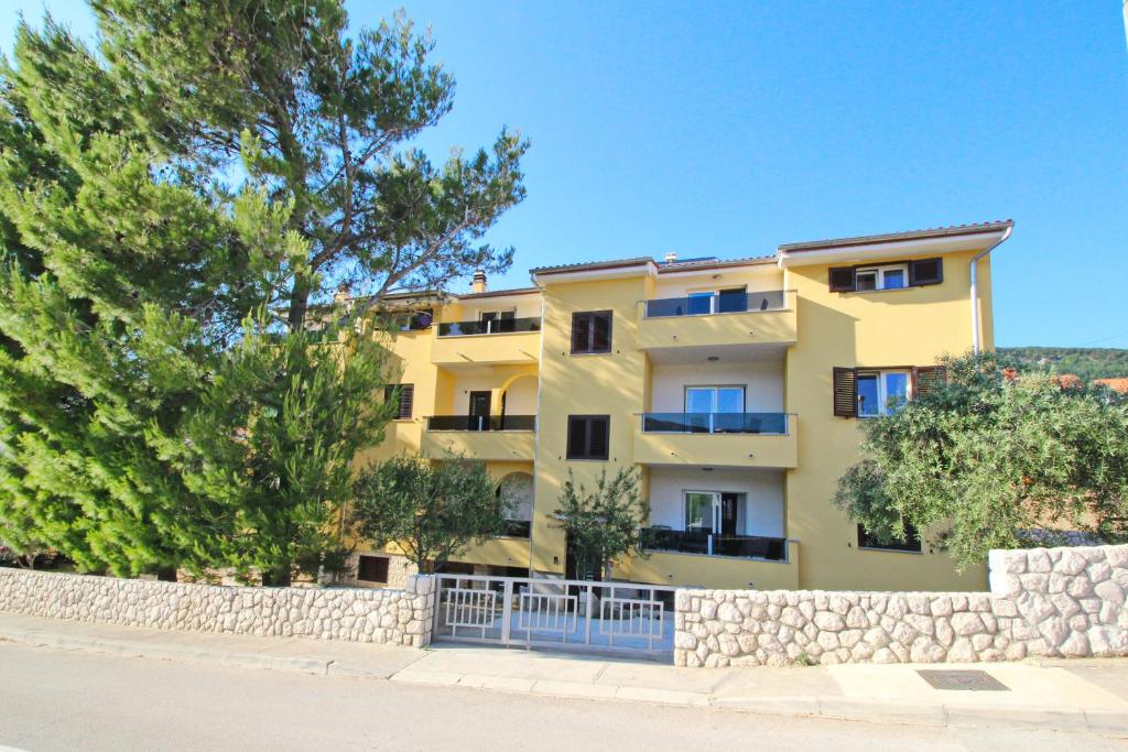 un edificio de apartamentos amarillo con valla y árboles en Sunshine Residence Baska en Baška