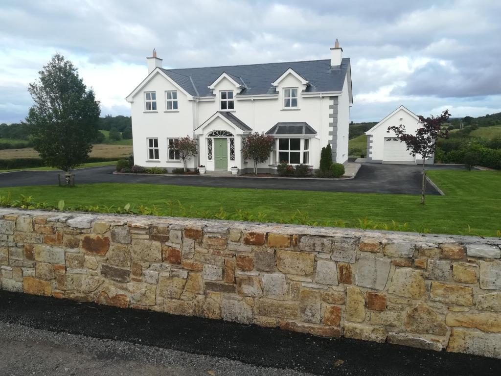 Cette grande maison blanche est dotée d'un mur en pierre. dans l'établissement The Meadows Guest House, à Ballintogher