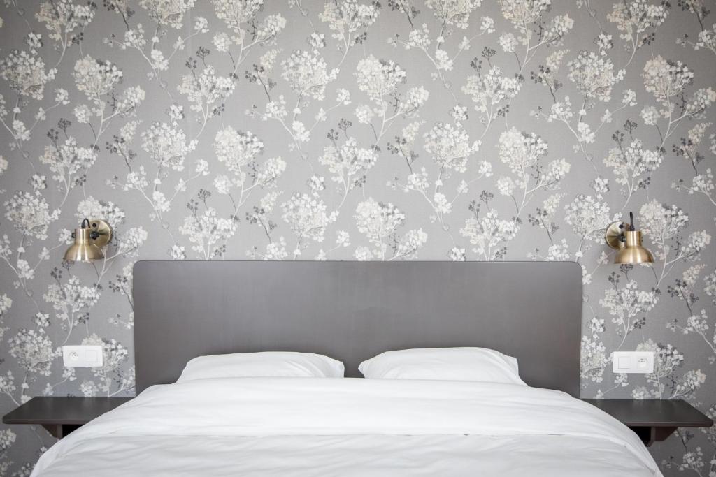 um quarto com uma cama com lençóis brancos e papel de parede floral em La Maison du Passavant (Gîte à la ferme) em Genappe