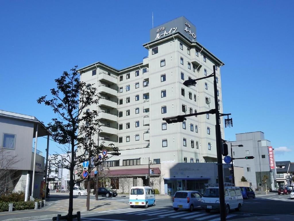 um edifício alto e branco com carros estacionados em frente em Hotel Route-Inn Shimada Ekimae em Shimada