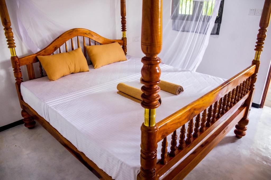 ein Holzbett mit weißer Bettwäsche und gelben Kissen in der Unterkunft Isuru Cabanas and Restaurant in Tangalle
