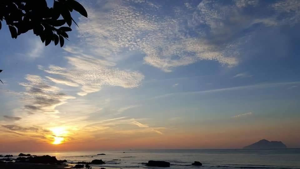 a sunset over the ocean with a mountain in the background at Ocean Sky Homestay in Toucheng