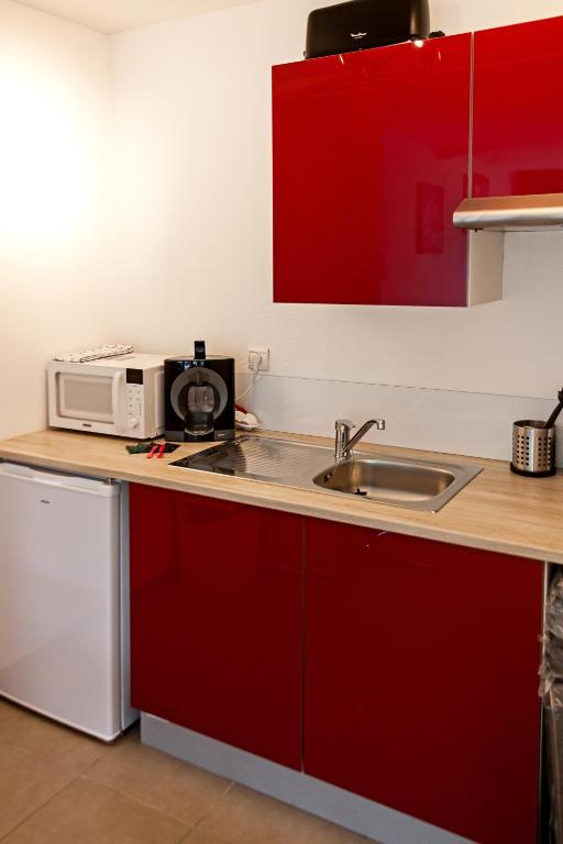 eine Küche mit roten Schränken, einer Spüle und einer Mikrowelle in der Unterkunft studio du botanique in Bayeux