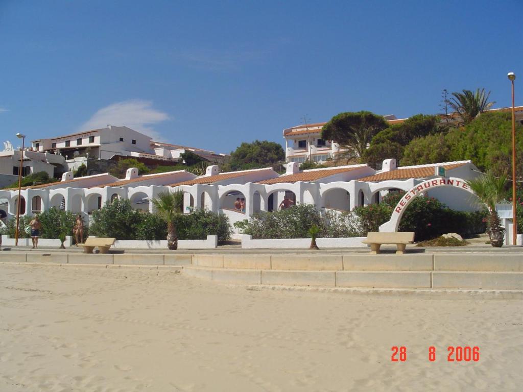 una fila de edificios blancos en una playa con bancos en Apartamentos LLorca en Platja de l’Almadrava