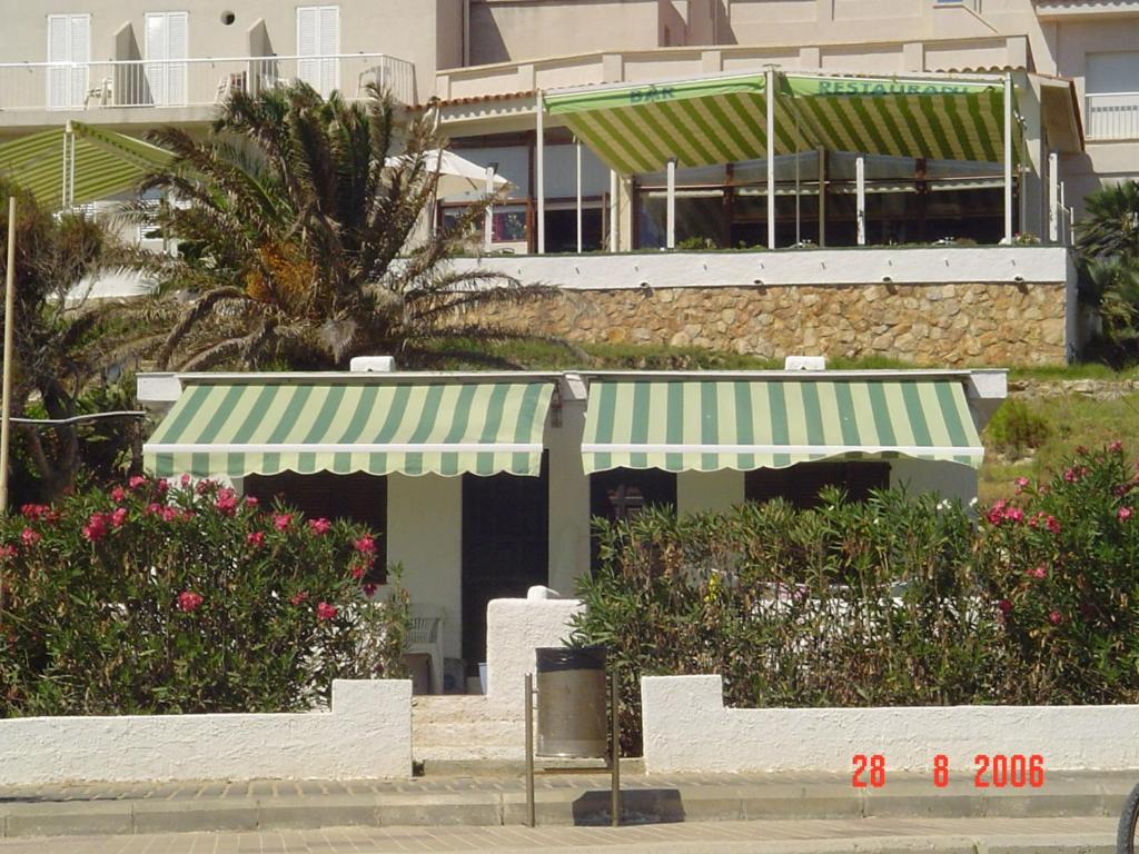 a building with a green and white awning and flowers at Apartamentos LLorca in Platja de l’Almadrava