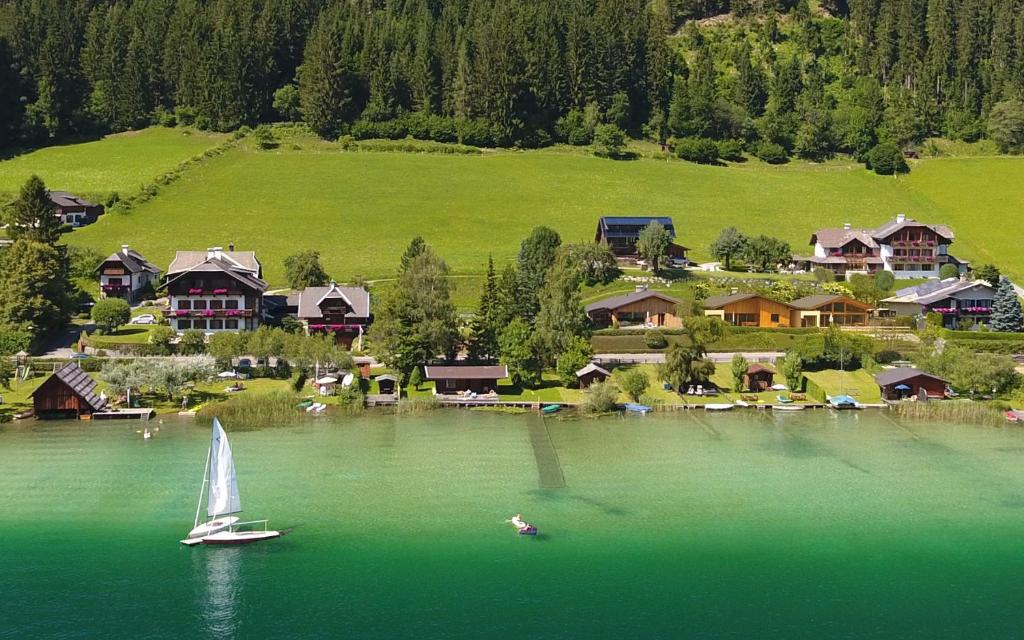 a sail boat in the water in front of a village at Ferienhof Obergasser und Bergblick in Weissensee