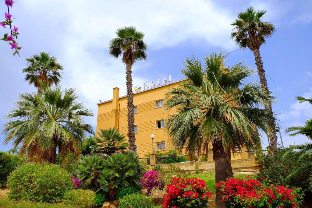 a yellow building with palm trees and flowers at Colleverde Park Hotel in Agrigento