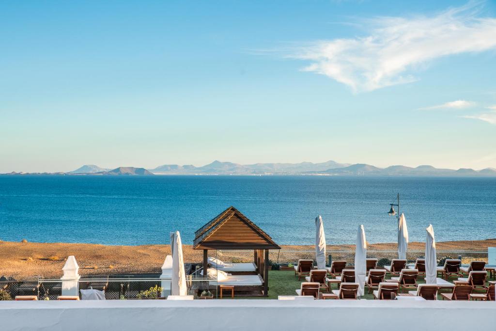 a beach with chairs and a gazebo and the ocean at Hotel LIVVO Volcán Lanzarote in Playa Blanca