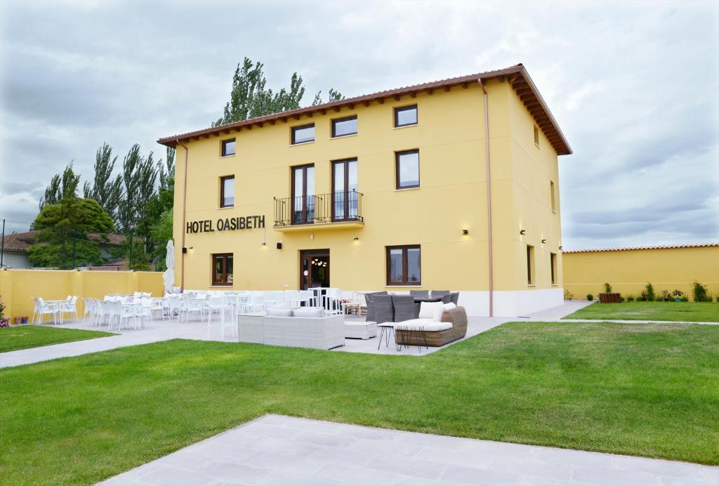 um grande edifício amarelo com mesas e cadeiras brancas em Hotel Rural Oasibeth em Frómista