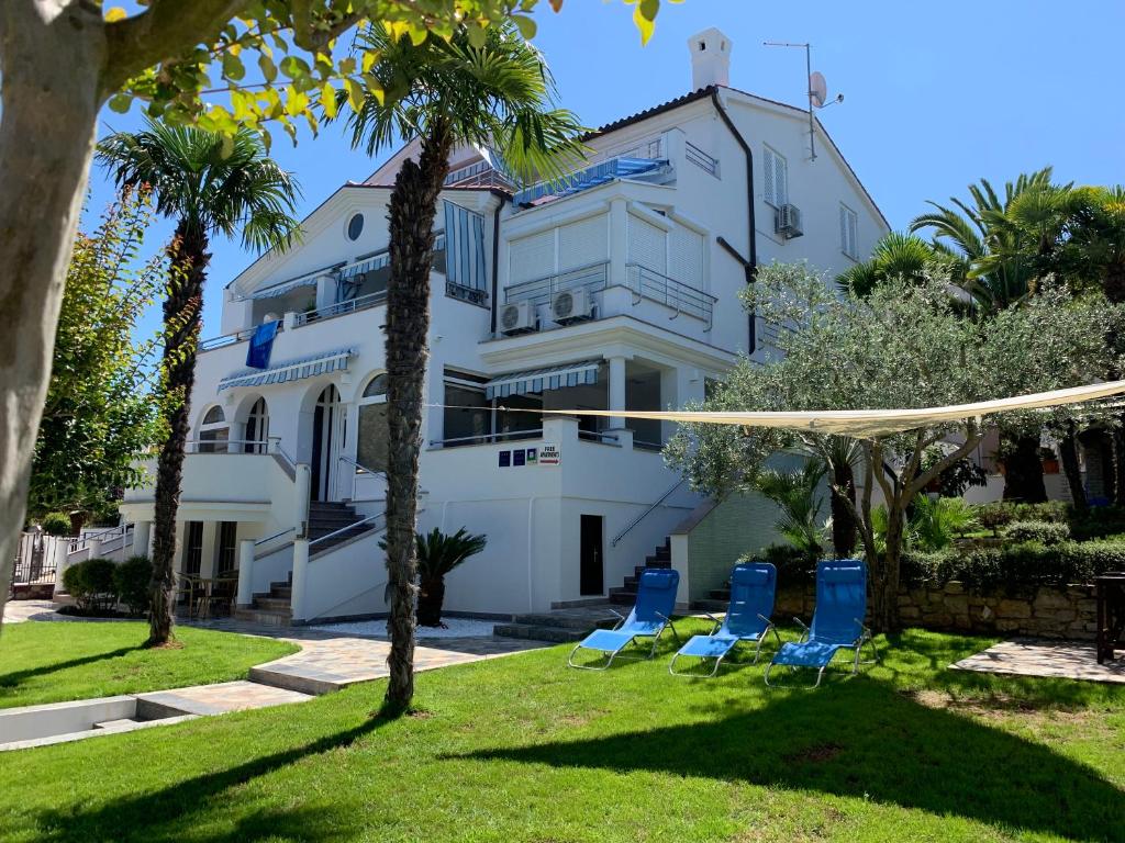 a white building with blue chairs and palm trees at Apartmani Auer in Pješčana Uvala