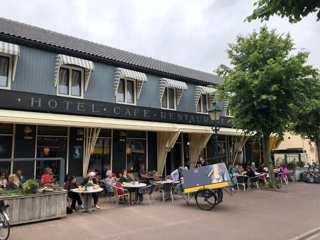 een groep mensen die aan tafels buiten een gebouw zitten bij Hotel Nap in West-Terschelling