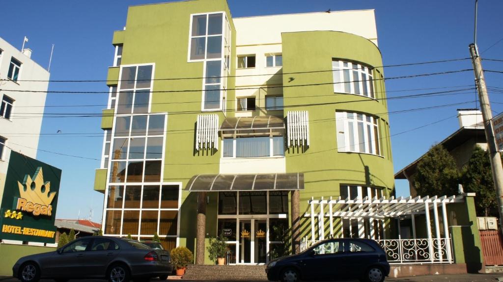 a green building with cars parked in front of it at Hotel Regat in Piteşti