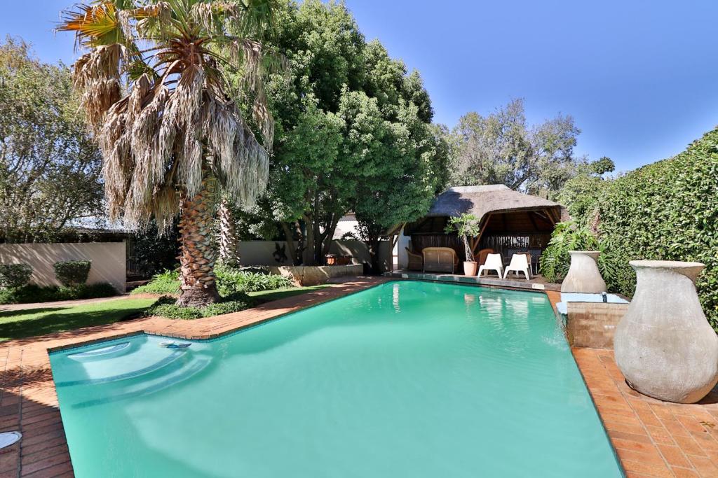 einen Pool mit einer Palme und einem Pavillon in der Unterkunft Fin and Feather Guest Lodge in Boksburg