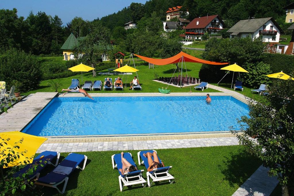 a swimming pool with chairs and umbrellas and people sitting at Hotel Restaurant Marko in Velden am Wörthersee