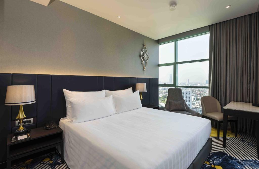 a hotel room with a bed and a desk and a window at Chatrium Hotel Riverside Bangkok in Bangkok