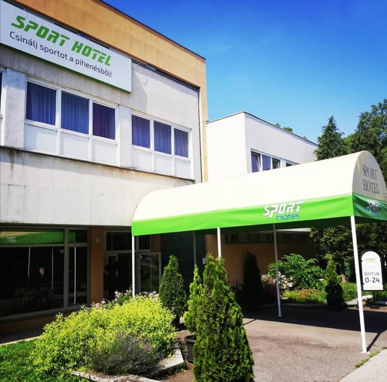 un bâtiment avec un parasol vert devant lui dans l'établissement Sport Hotel, à Tatabánya