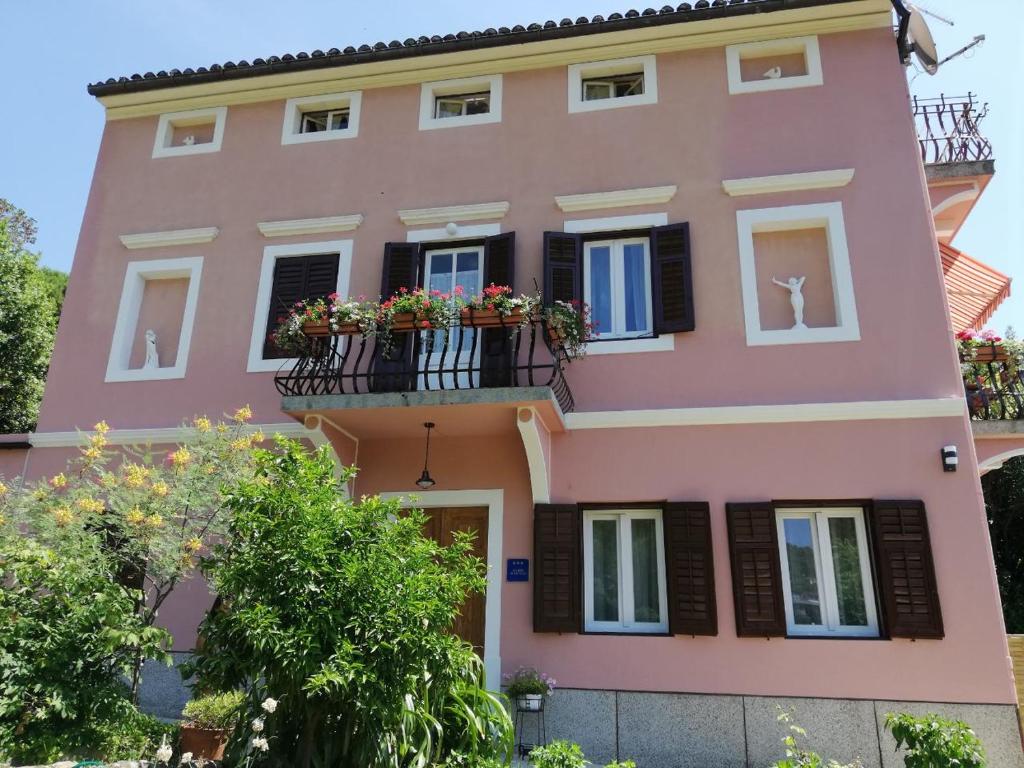 una casa rosa con flores en los balcones en APARTMAN LUŠETIĆ en Opatija