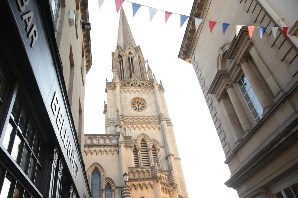 un campanario de la iglesia con una torre del reloj con banderas en St Christopher's Inn Bath, en Bath