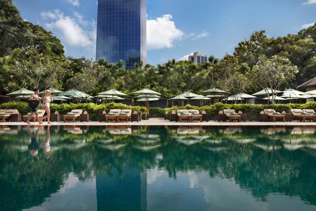 una piscina con sillas y sombrillas en un complejo en The Sukhothai Bangkok, en Bangkok