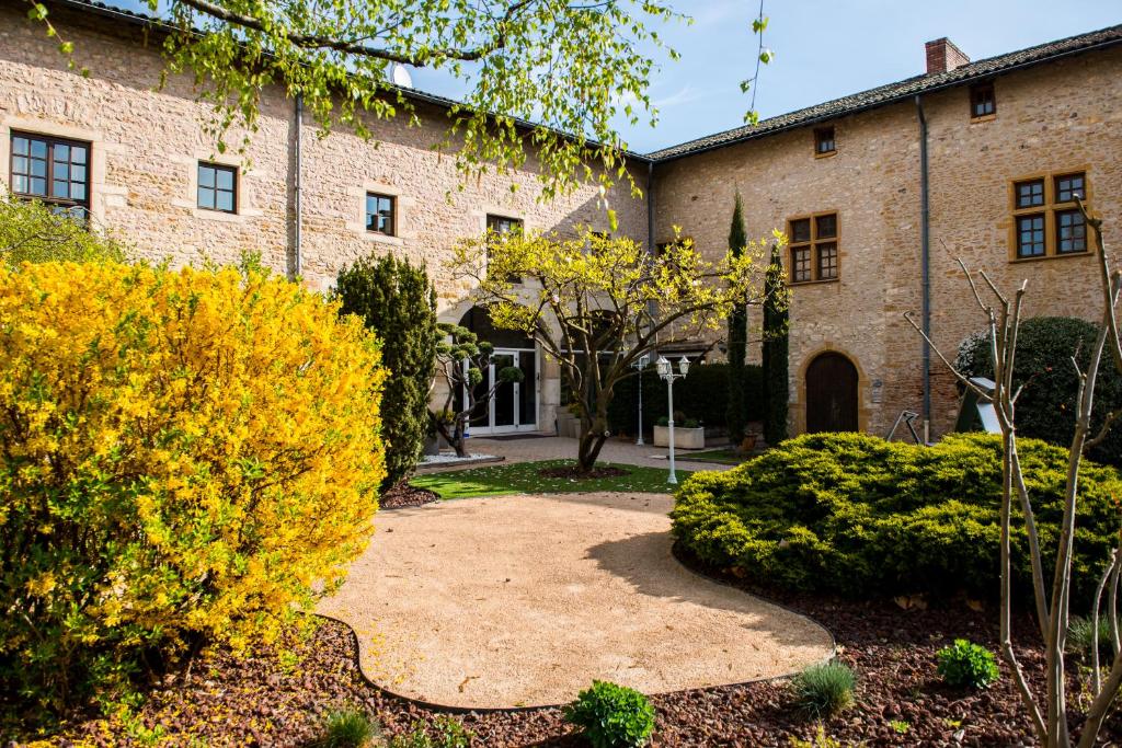um grande edifício de tijolos com um jardim em frente em Hostellerie la Ferme du Poulet et son restaurant em Villefranche-sur-Saône