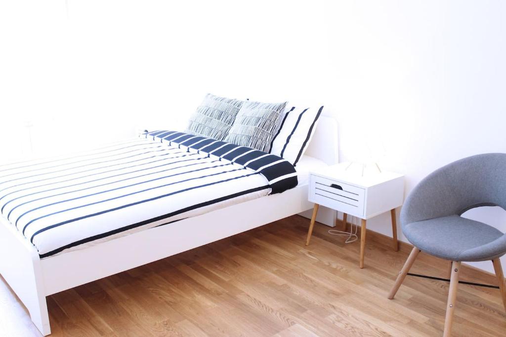 a white bedroom with a bed and a chair at NEW Central Light Apartment with Private Parking in Novi Sad