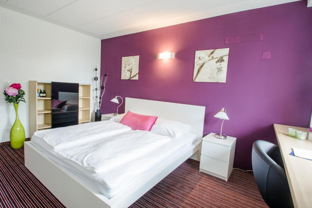 a bedroom with a white bed with a purple wall at College Garden Hotel in Bad Vöslau