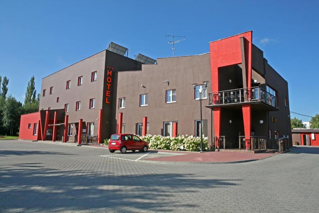 un'auto rossa parcheggiata di fronte a un edificio di Hotel Altamira a Piotrków Trybunalski