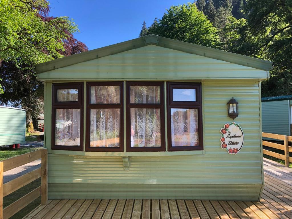 a green building with windows on a wooden deck at Lyndhurst 39 in Dunoon