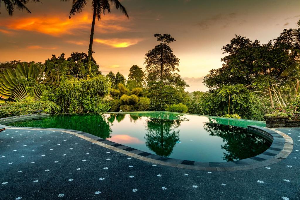 a pool in the middle of a garden with trees at Tanah Merah Art Resort in Ubud