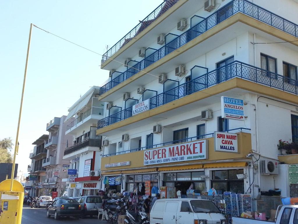 a large white building with cars parked on a street at Angelos Hotel in Agios Nikolaos