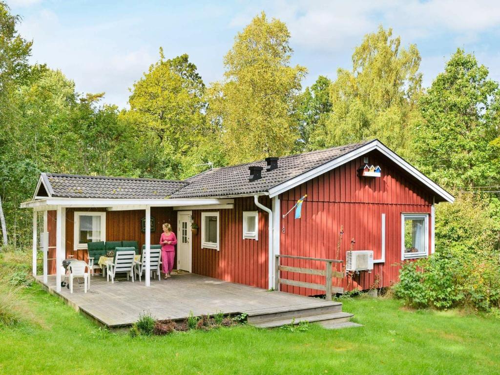 a woman standing on the porch of a red house at Two-Bedroom Holiday home in Hallabro 3 in Hallabro