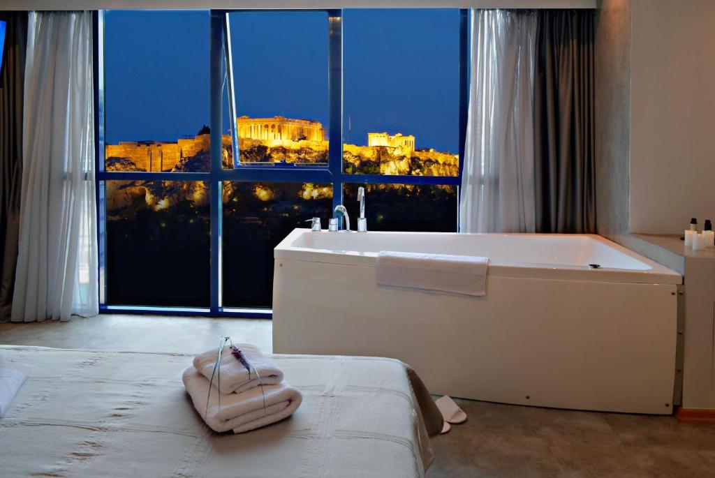 La salle de bains est pourvue d'une baignoire et d'une grande fenêtre. dans l'établissement BEAUTIFUL PEOPLE SUITES ATHENS ACROPOLIS VIEW, à Athènes