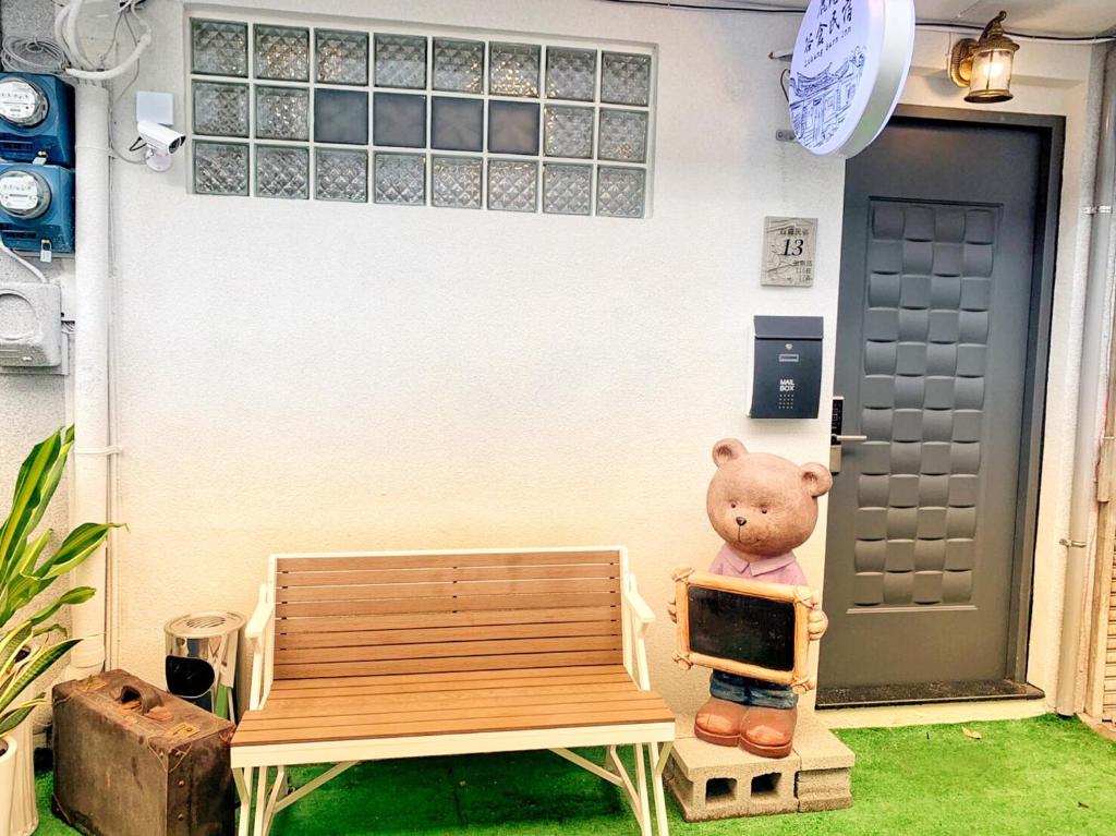 un oso de peluche sentado en un banco frente a una puerta en Lukang Barn Inn, en Lukang