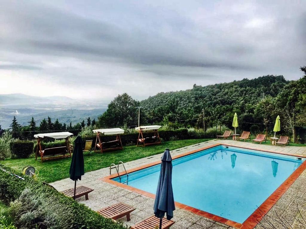 a swimming pool with chairs and umbrellas next to a mountain at Casa Mazzoni in Roccastrada