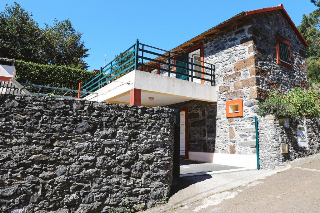 a house with a stone wall and a balcony at Raposeira Chloe T2 in Fajã da Ovelha