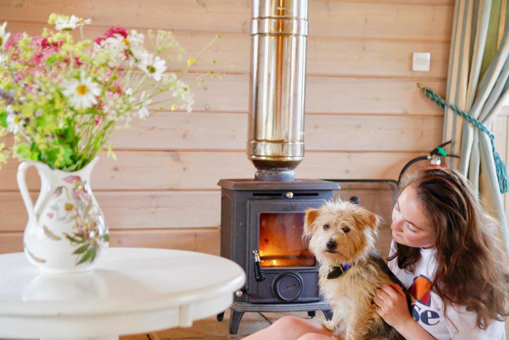 a young girl is petting a dog in front of a stove at Lapwing, Skylark & Curlew Seaside Chalets in Kirkbean