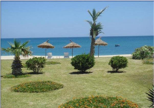 una playa con sombrillas, palmeras y el océano en Villa Eden Park sur la plage, en Fnidek