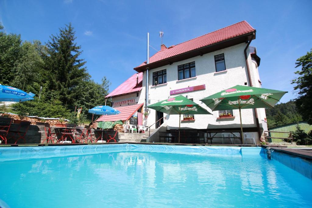 a swimming pool in front of a building with umbrellas at Penzion Paseky U Zapadlych vlastencu in Paseky nad Jizerou