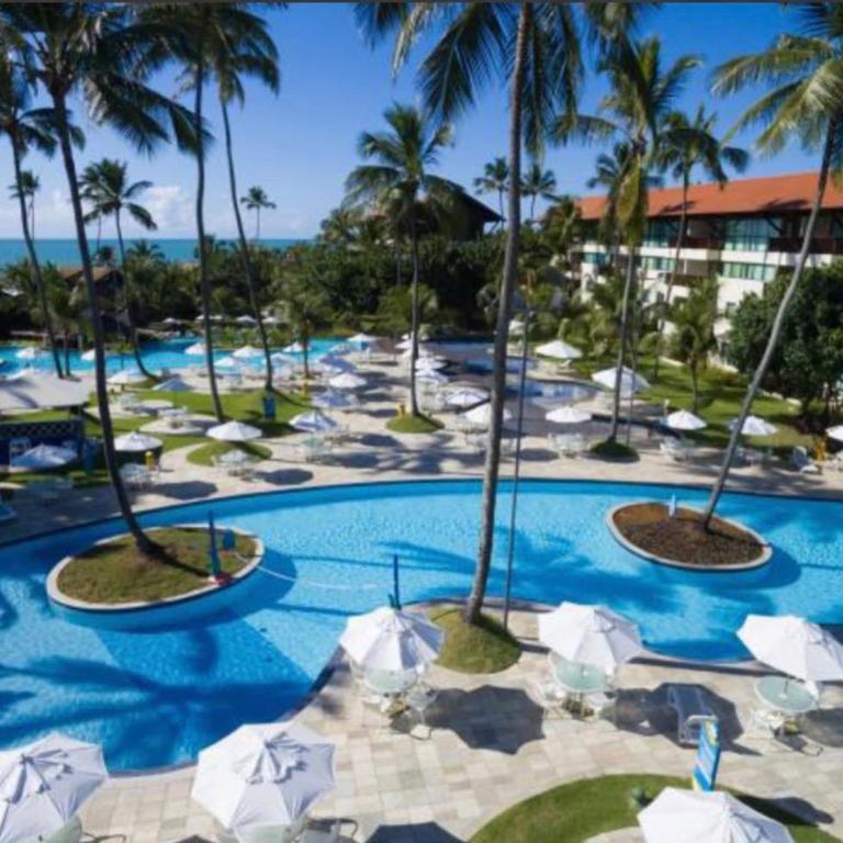 a resort with a pool with umbrellas and palm trees at Flat 2 quartos Resort Marulhos Porto de Galinhas C401 in Porto De Galinhas