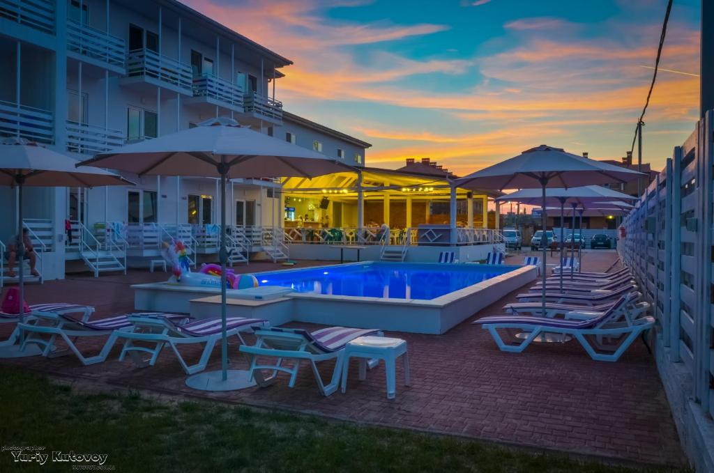 a resort pool with chairs and umbrellas at sunset at Family Hotel Happy INN in Zatoka